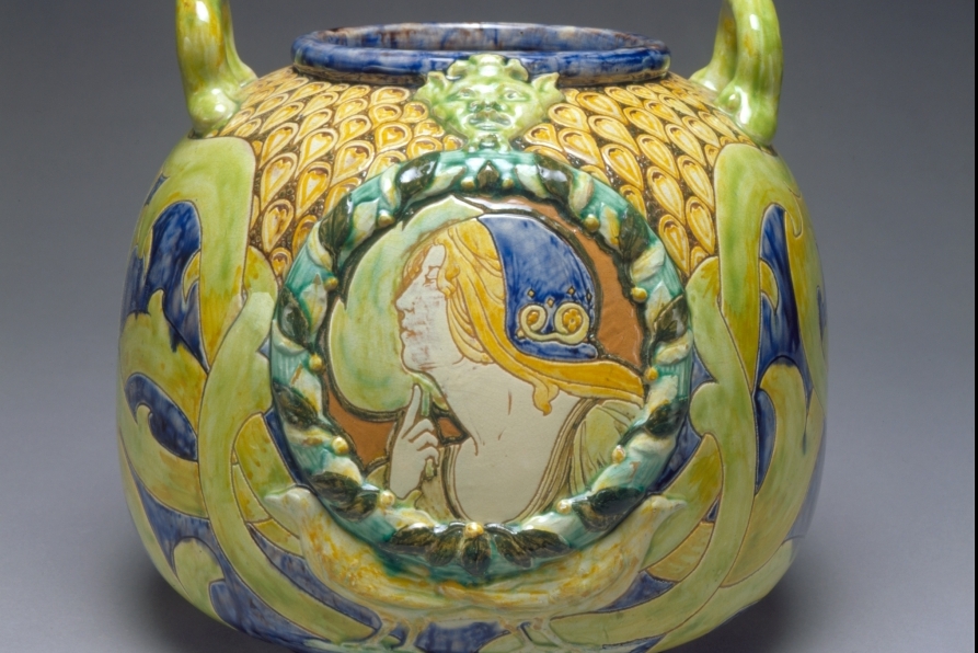 Urn featuring side profile of woman's face, decorated in yellow, bright light green and dark blue patterns. Featured image for Collections.