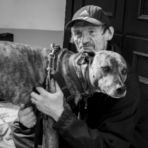 black and white photograph from Mac Davenant's Outsider's series on a man in a baseball cap holding a dog