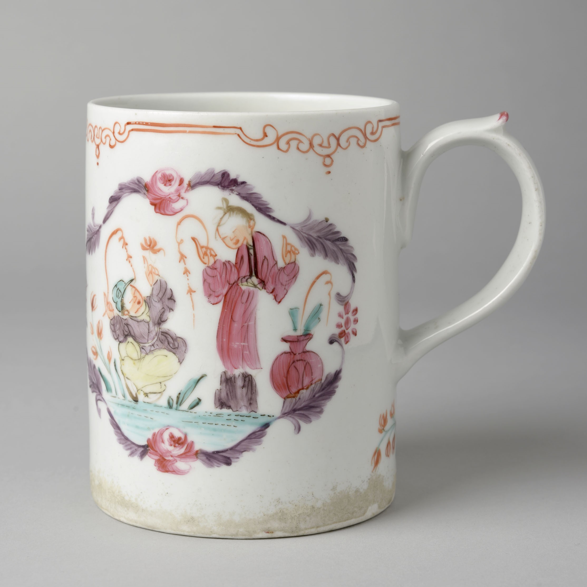 A white porcelain cup decorated with a cameo featuring two men; however it's unclear what they're doing as the cup is turned to the side.