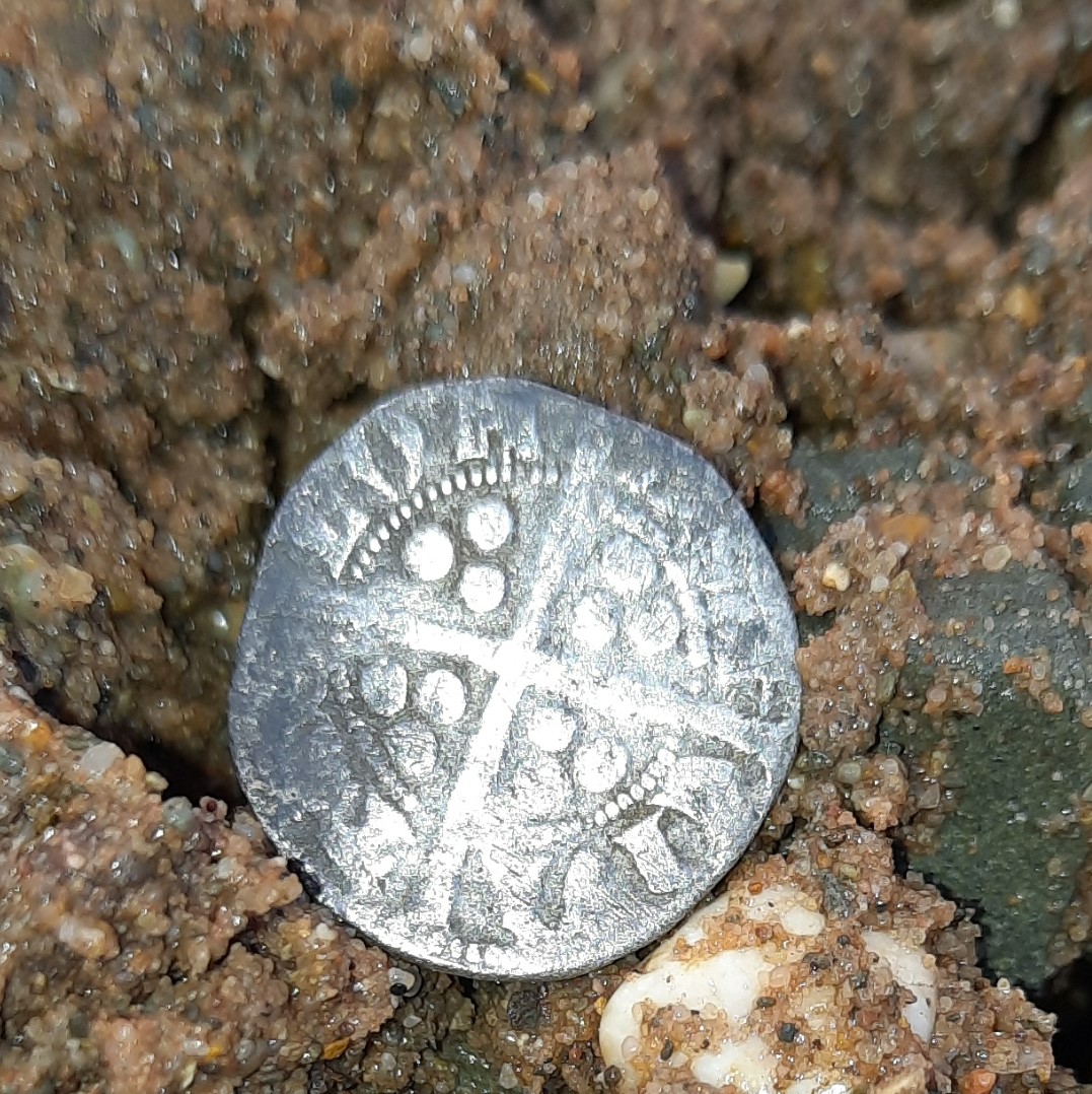 ancient faded silver coin sitting on pebbles and sand on a beach