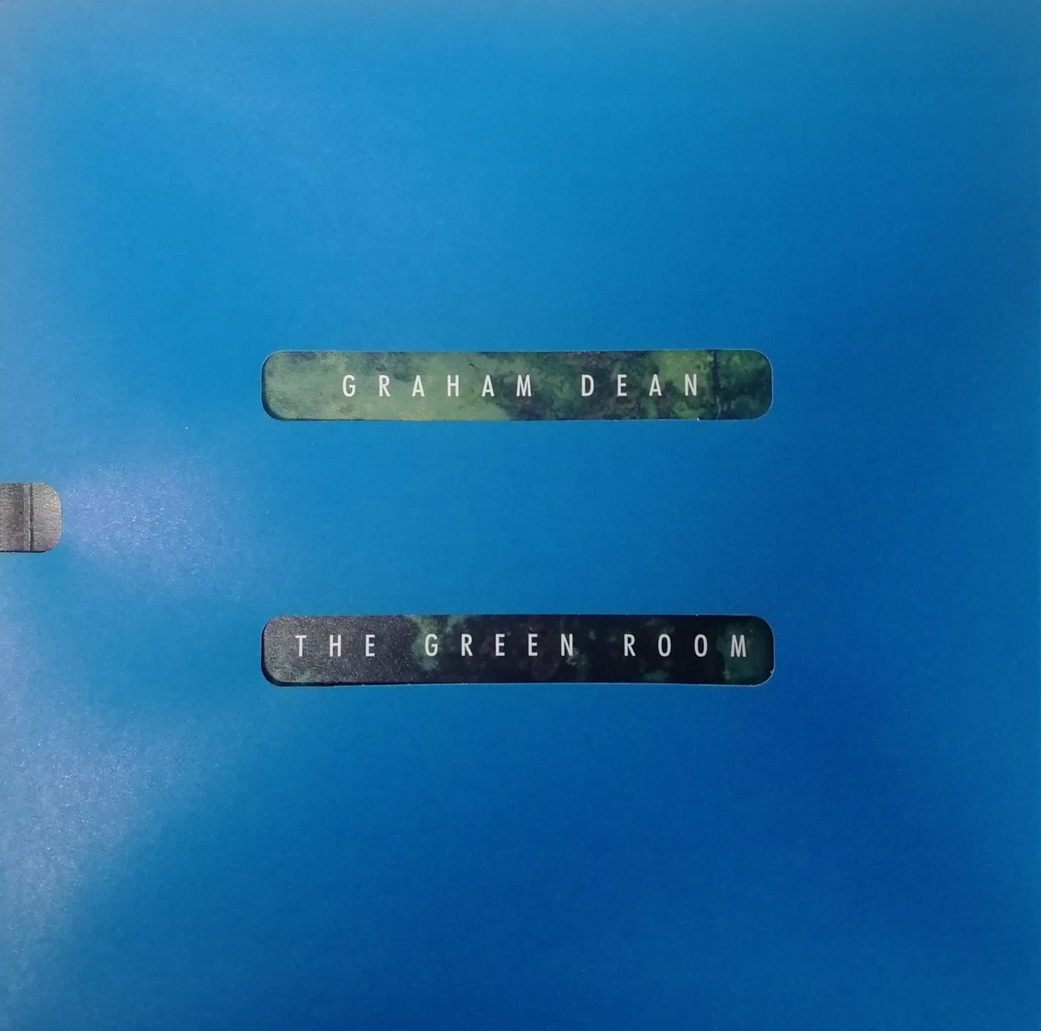 Image of an exhibition catalogue in a blue sleeve. There are two holes in the blue where we can see a green background and the words "Graham Dean" and "The Green Room".