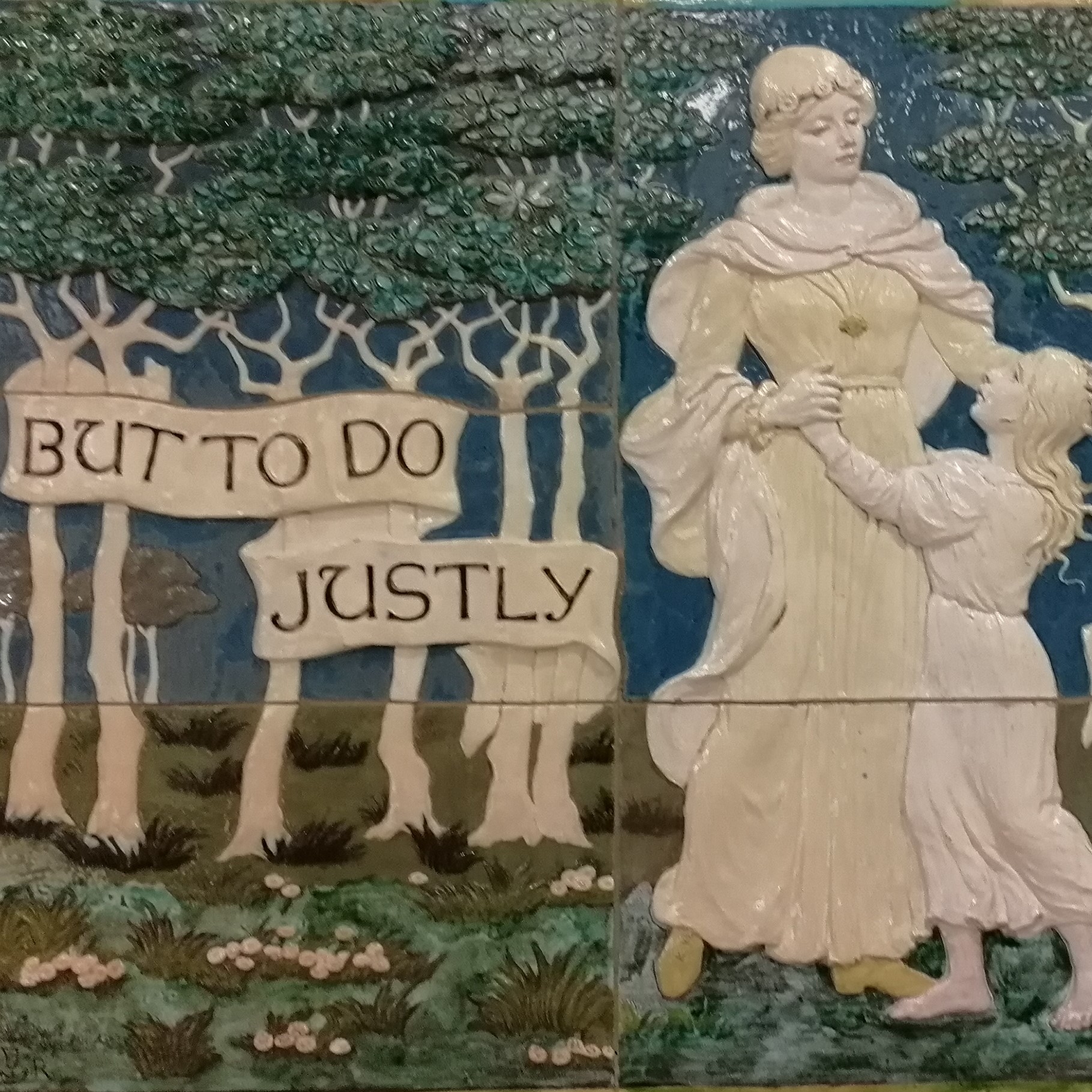 A section of a coloured wall tile. On the left are a group of trees with a banner over them which reads "but to do justly". On the right a woman in a long dress and cape is dancing with a small child.